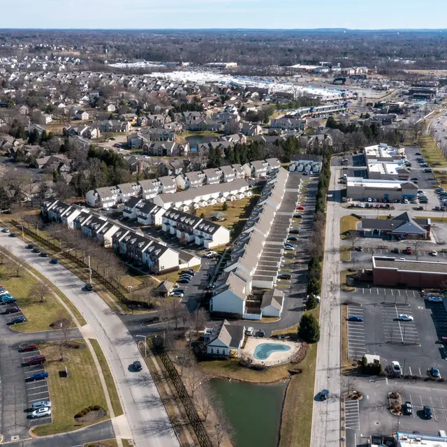 Aerial view of a suburban area featuring residential buildings, parking lots, roads, and green spaces.