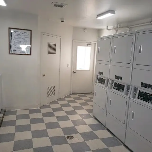 Interior view of a laundry room featuring several washing machines and dryers along with a door leading outside.