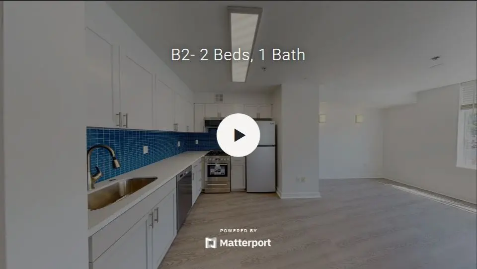 A modern kitchen with white cabinets, stainless steel appliances, and a blue tiled backsplash, featuring a play button overlay.