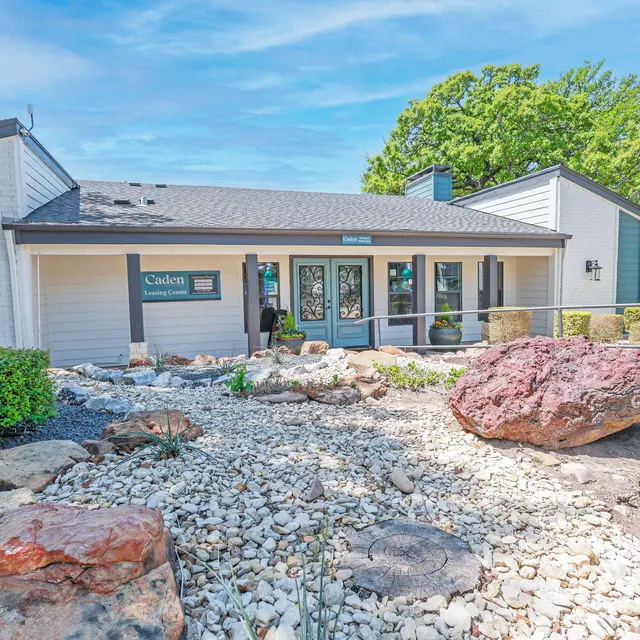 A well-maintained apartment complex entrance surrounded by landscaped rocks and greenery under a clear blue sky.