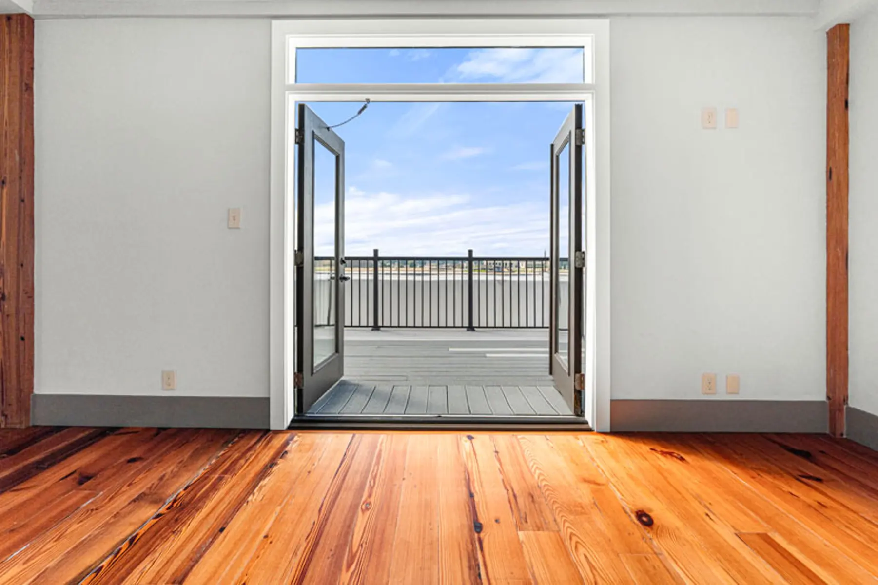 Interior view of a room with hardwood floor leading to double doors opened to a balcony.