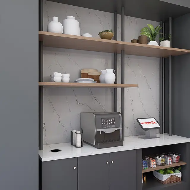 A modern kitchenette featuring open shelves with decorative items, a coffee machine, and a countertop. The wall is gray with framed art pieces and a clock.