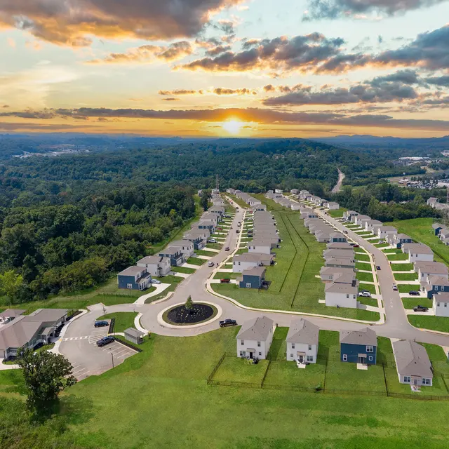 Aerial view of a housing development with rows of houses, a pool area, and a sunset sky in the background.