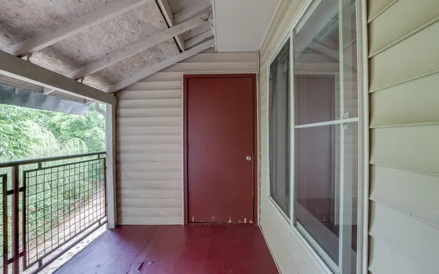 A balcony area showing a door, window, and railing overlooking greenery.