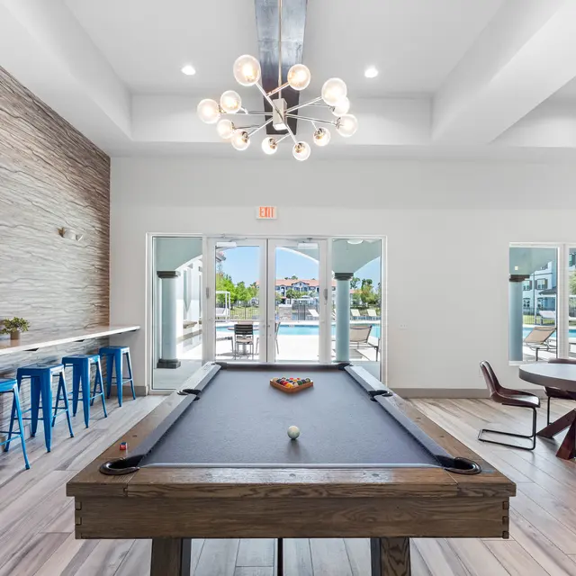 Modern Game Room Featuring Pool Table A modern game room featuring a pool table, bar stools, and large glass doors leading to an outdoor area with a pool.