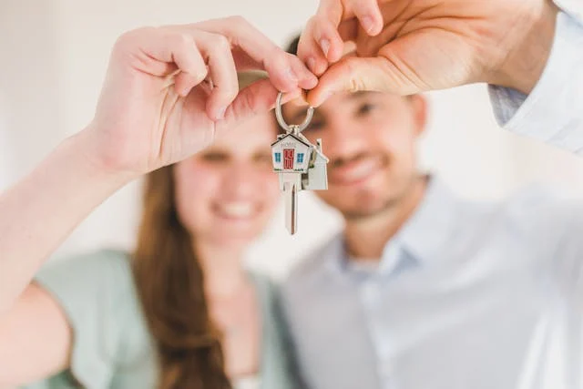 A couple smiling and holding a key with a small house-shaped keychain in front of them.