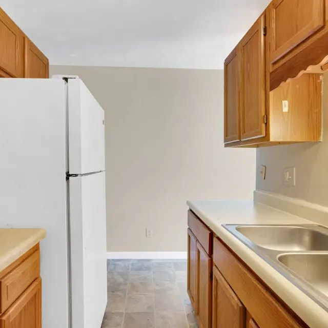 A small kitchen featuring wooden cabinets, a white refrigerator, and a double sink.