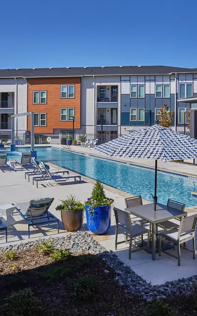 Exterior view of a modern apartment complex featuring a swimming pool area with lounge chairs and umbrellas.