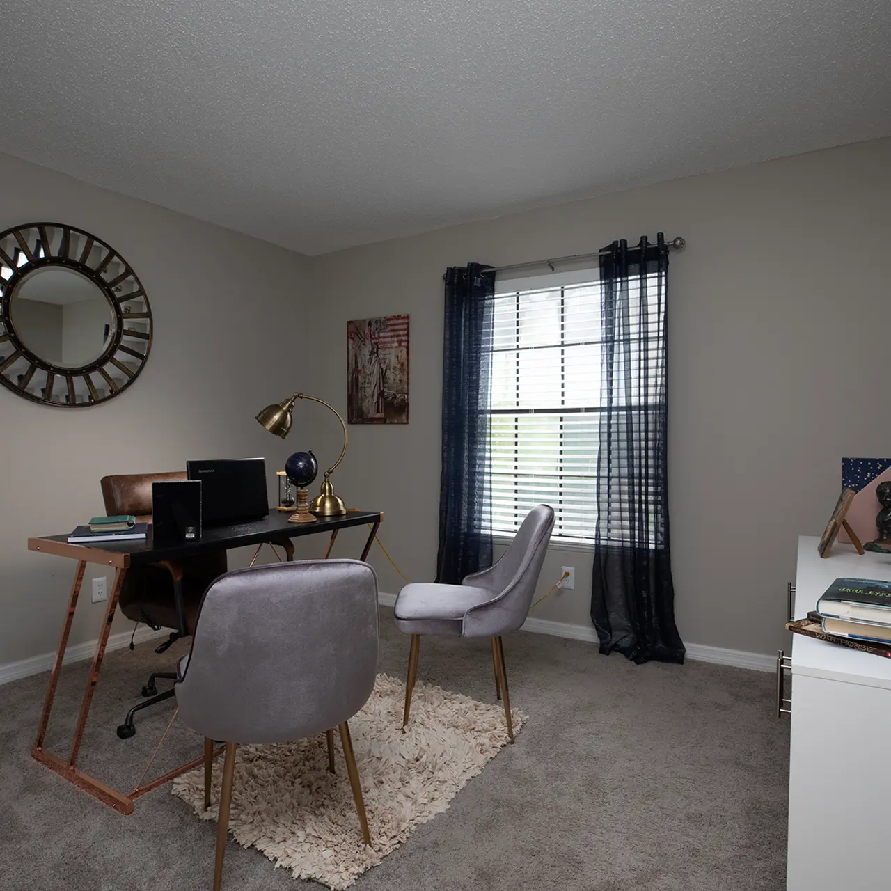 A modern home office with a stylish desk, two chairs, and large windows dressed with dark blue curtains.