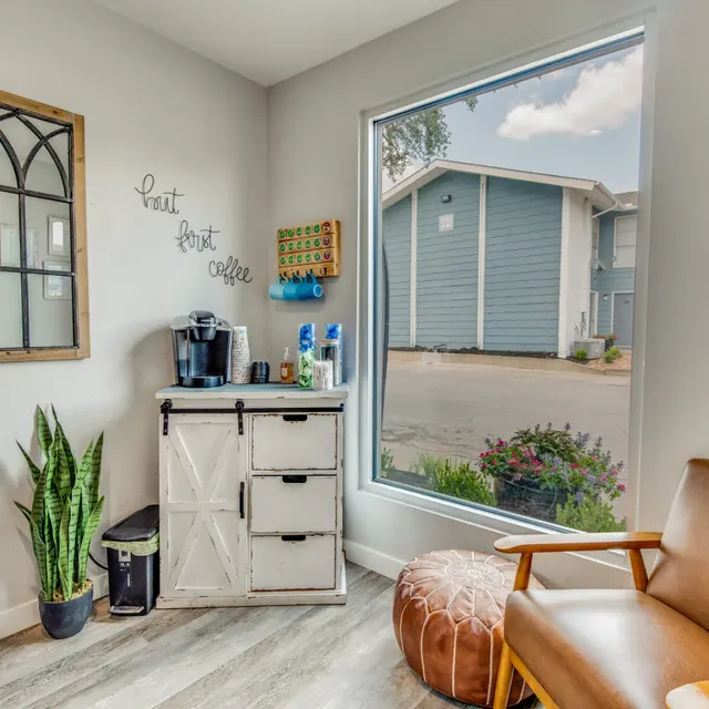 A cozy corner of a cafe with a coffee machine, a chair, and a potted plant next to a large window showcasing the outside view.