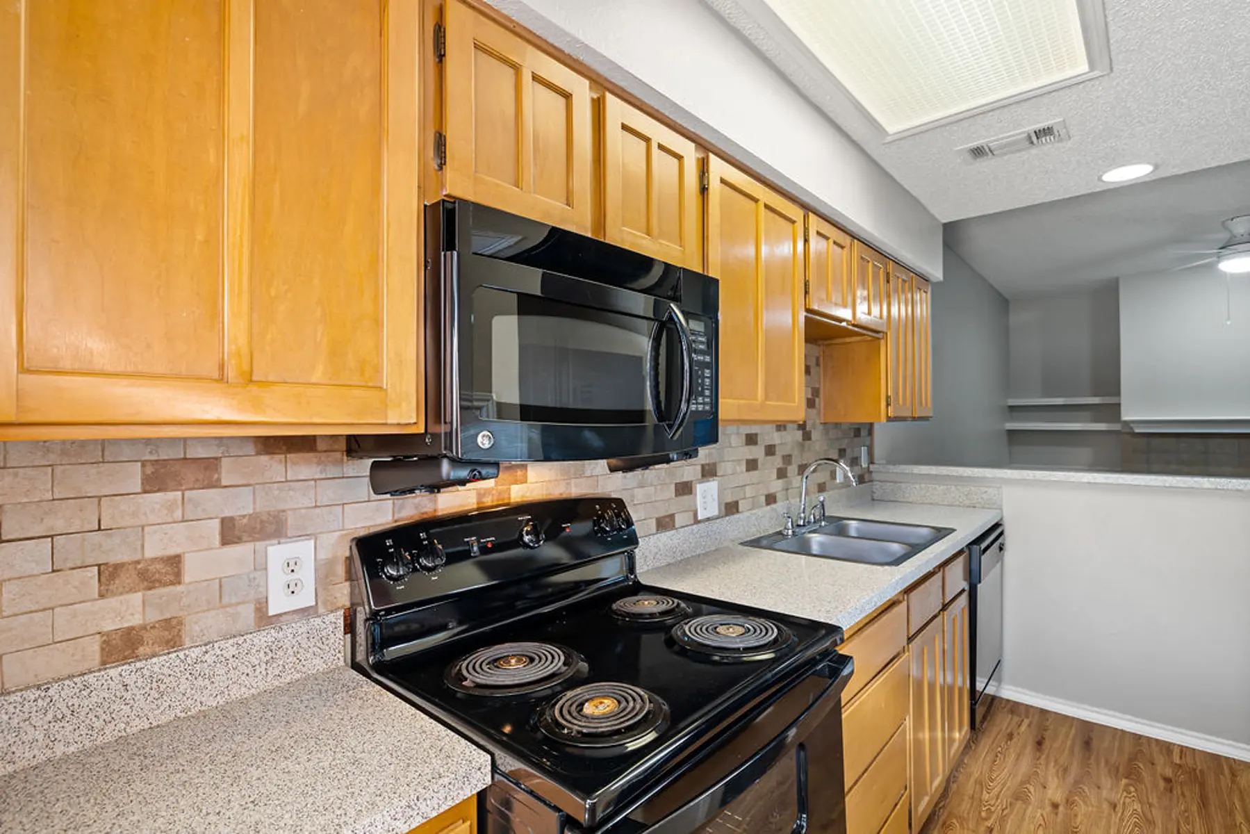 Stylish Modern Kitchen A modern kitchen featuring wooden cabinets, a black stove, a microwave, and a sink, with a tiled backsplash and a countertop.