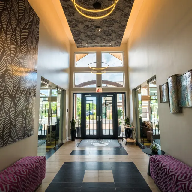 A contemporary hallway featuring stylish benches, decorative wall art, and a large glass entrance door that leads outside.