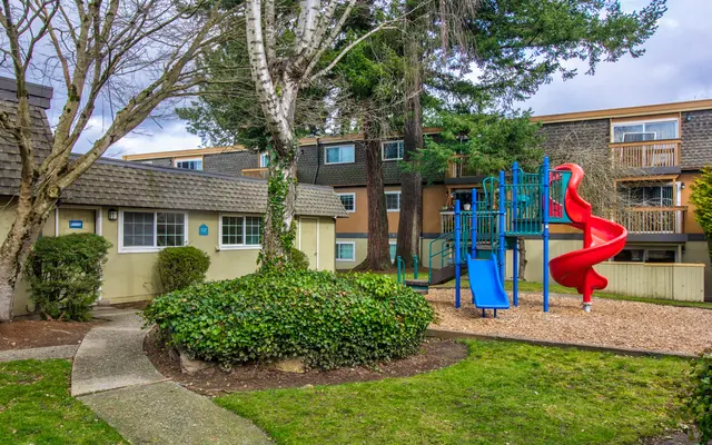 Residential Playground Area Playground featuring a blue slide and red spiral slide surrounded by trees and residential buildings.