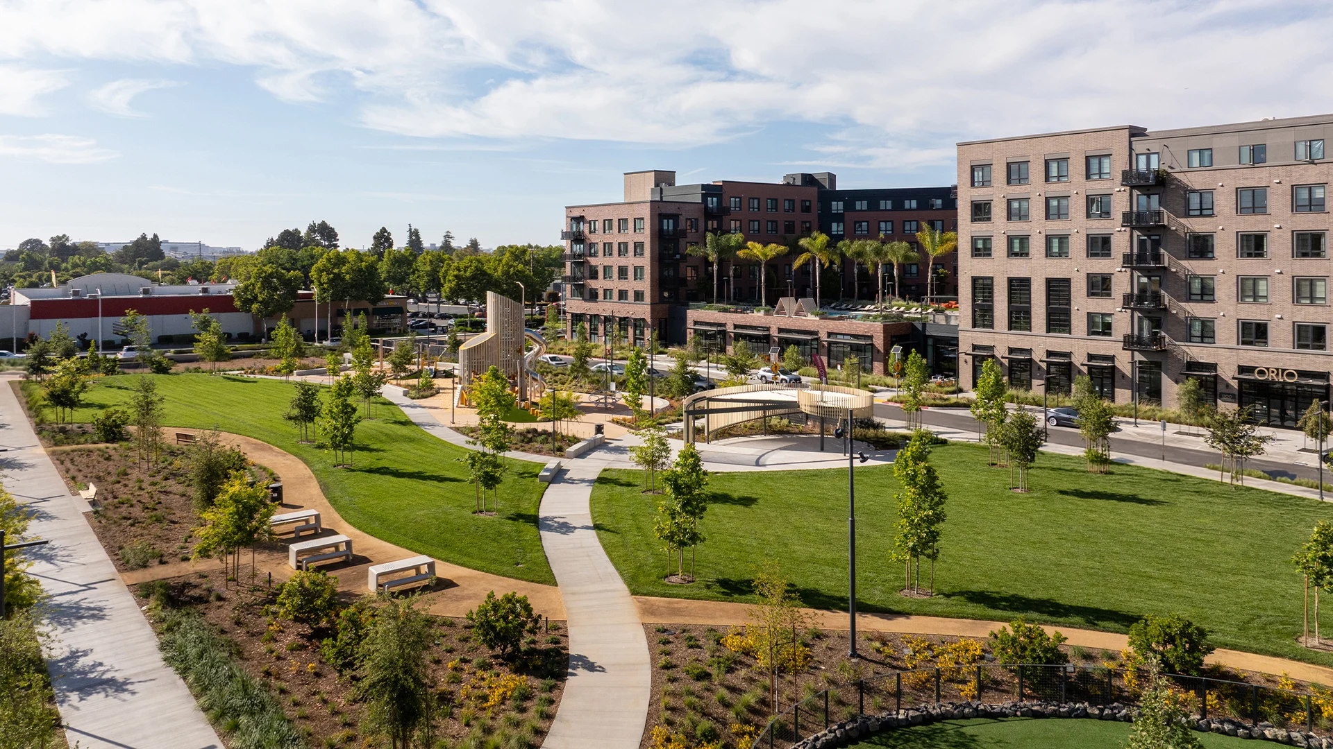 Community Urban Park with Playground A modern urban park featuring a children's playground, walking paths, and green lawns bordered by new buildings.