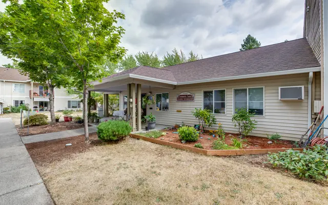 A well-maintained community building with a porch, surrounded by greenery and landscaped areas. Healthy trees and shrubs adorn the space, contributing to a welcoming atmosphere.