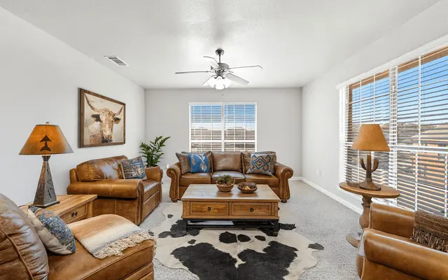 A well-decorated living room with leather furniture, a coffee table, large windows, and decorative lamps.