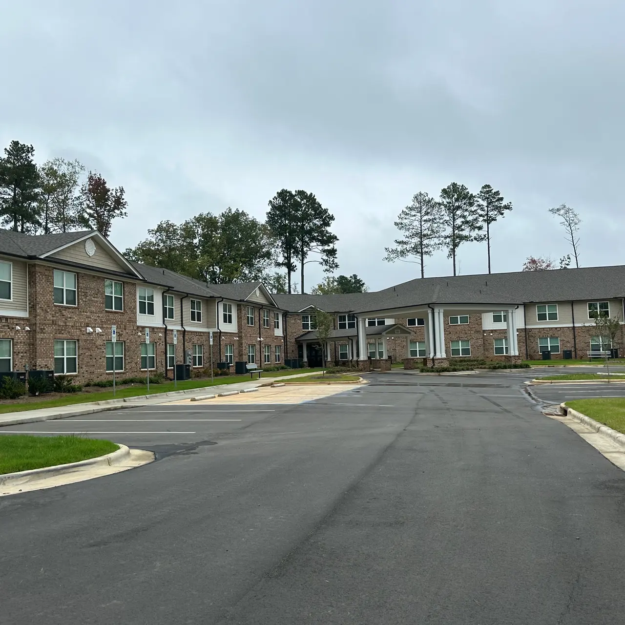 A view of a modern housing complex featuring two buildings, paved pathways, and landscaping, captured on an overcast day.
