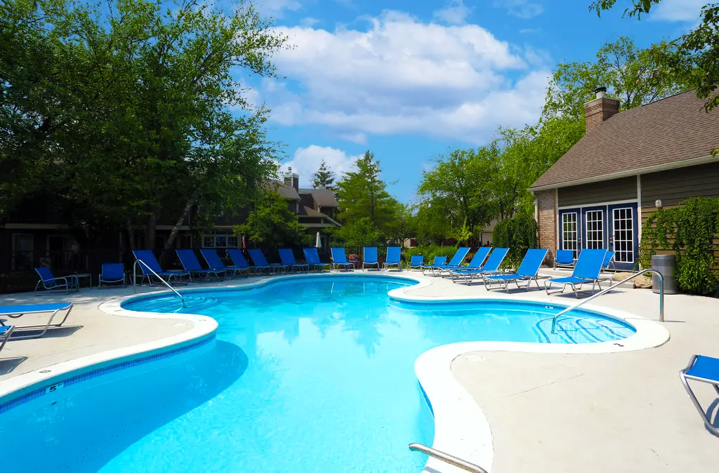 Swimming Pool Area A serene swimming pool area surrounded by lounge chairs and lush greenery under a blue sky with clouds.