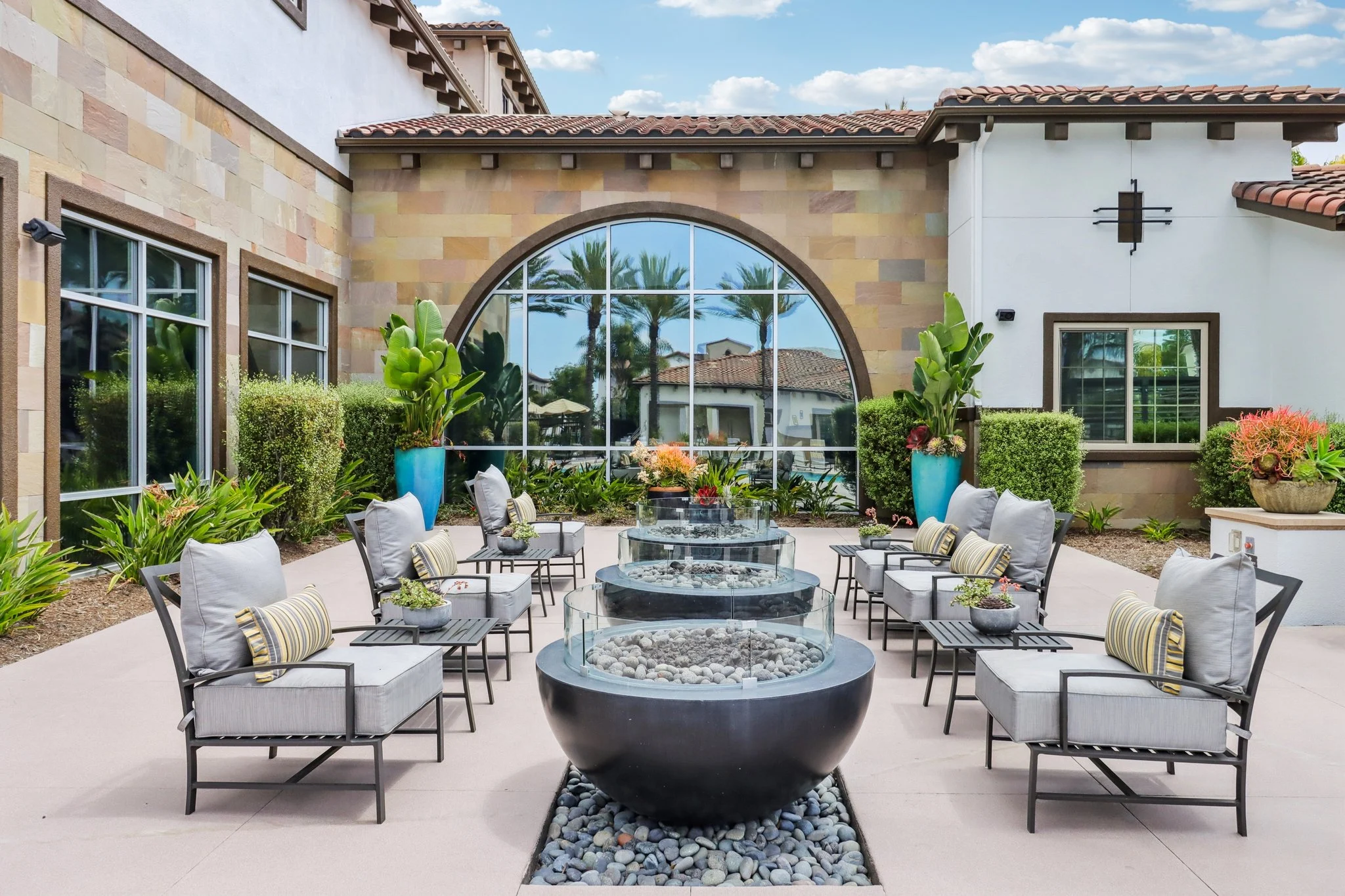 An inviting outdoor lounge area featuring comfortable seating, a central water feature, and lush greenery surrounded by walls with large windows.