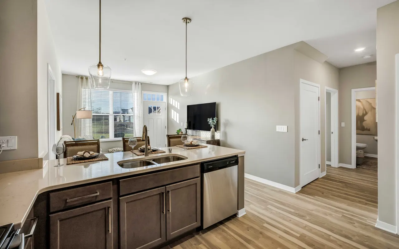 A modern kitchen with a breakfast bar, stainless steel appliances, and a living space featuring large windows and contemporary furniture.