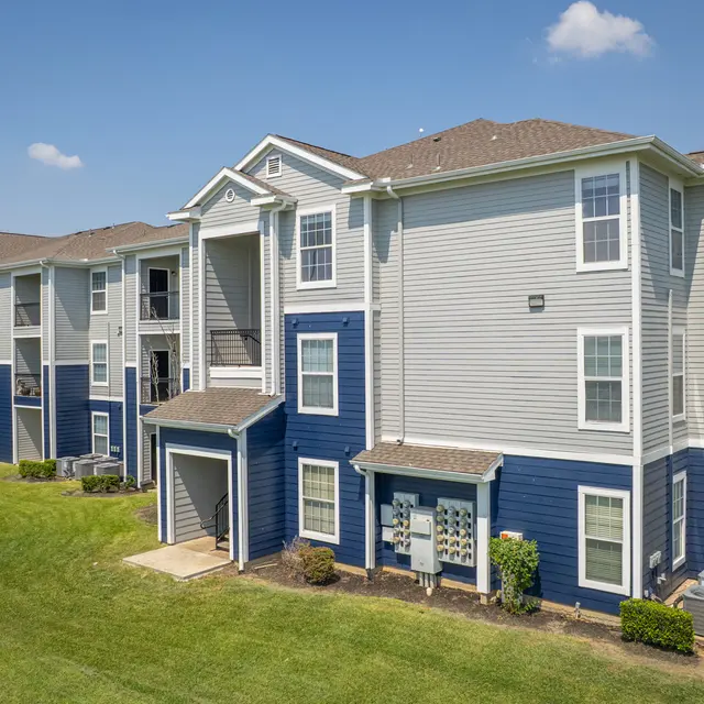 Modern Apartment Complex A modern apartment complex featuring buildings with blue and grey siding, surrounded by well-maintained lawns and greenery under a clear blue sky.