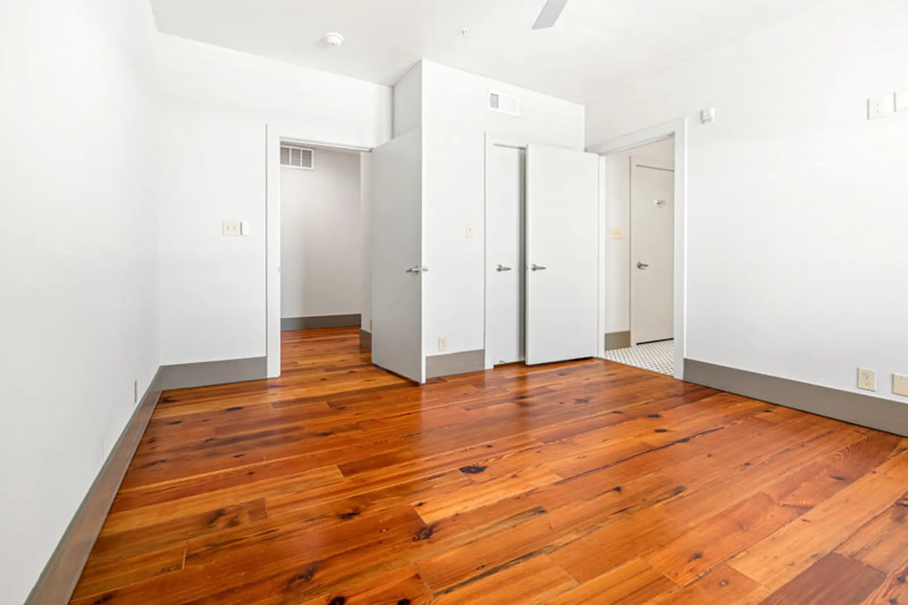 Empty bedroom featuring wooden floors and white walls with doors leading to other rooms.