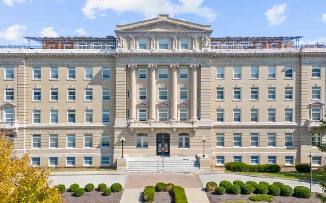 Historic Building Front View A historic building with a classic architectural design, featuring multiple windows and a prominent front entrance with stairs. The building is surrounded by manicured lawns and trees.