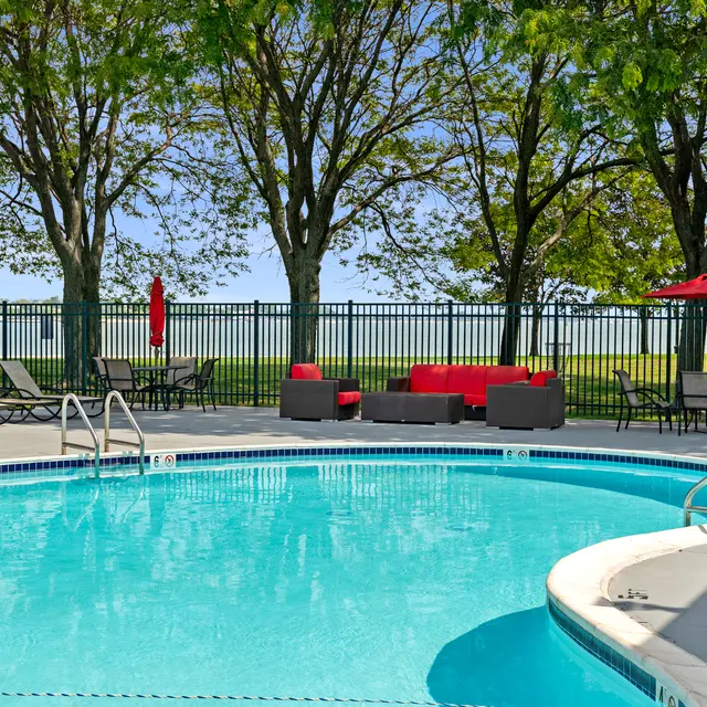 A swimming pool surrounded by lounging chairs and shaded seating areas beneath trees.