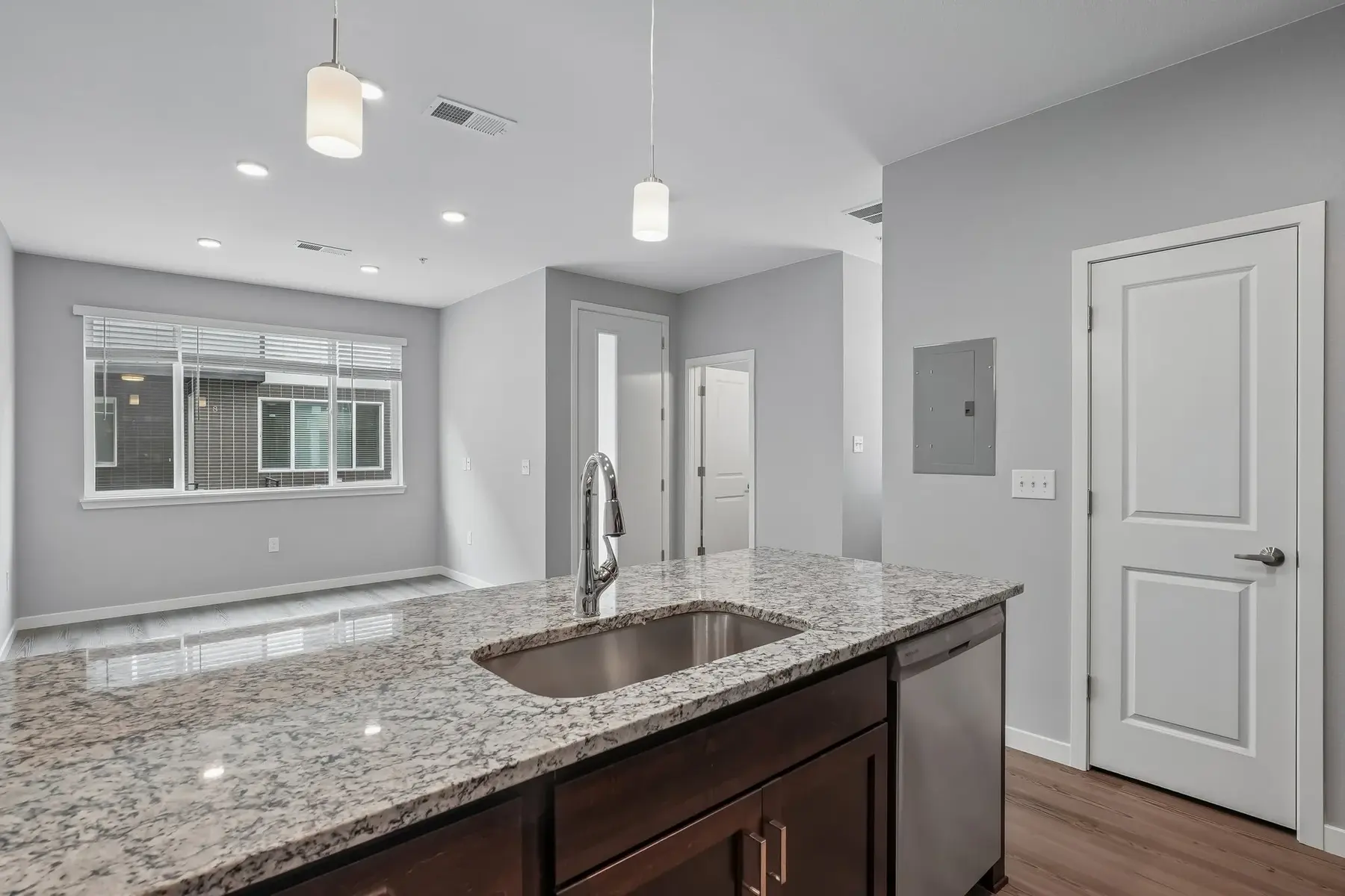A modern kitchen area featuring a granite countertop, a sink, and an open layout leading to a living space with large windows.