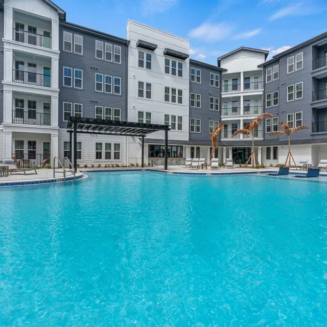 Modern Apartment Complex Pool A modern apartment complex with a large swimming pool surrounded by lounge chairs and shaded areas.