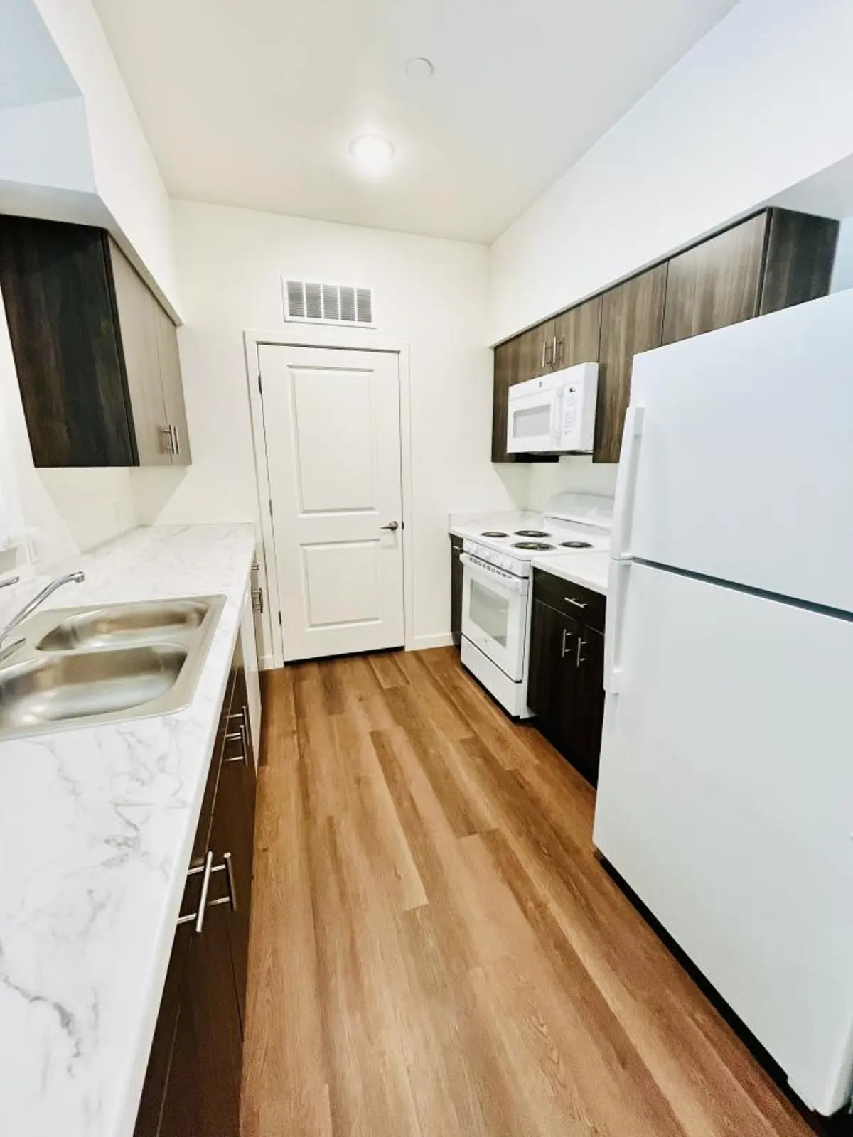 Kitchen with dark cabinets, white appliances and a light countertop.