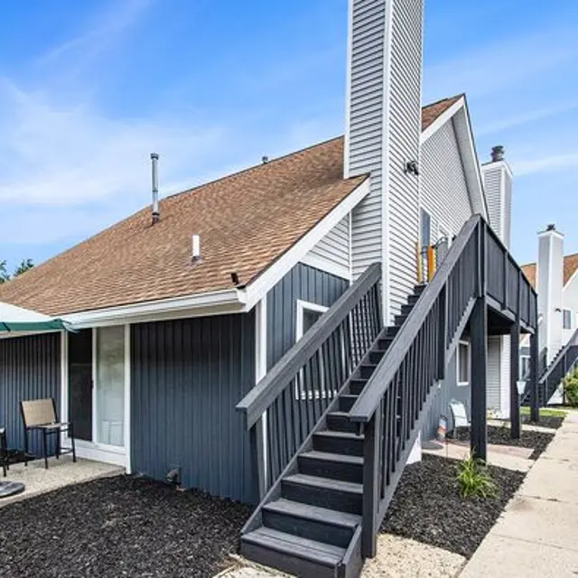 Exterior view of a townhouse complex with wooden stairs and a chimney under a blue sky.