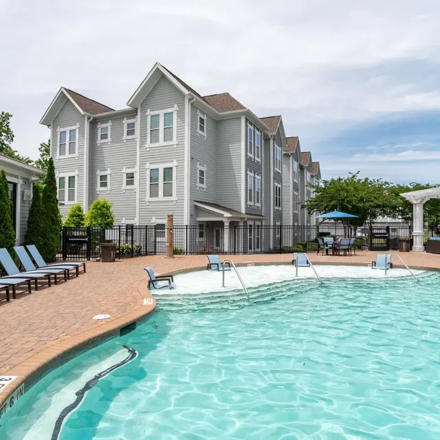 A view of a luxury apartment complex with a swimming pool surrounded by lounge chairs and landscaped gardens.