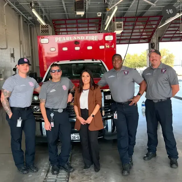 A group of five firefighters standing in front of a fire truck at the Pearland Fire Department station. They are dressed in uniforms and are smiling for the photo.