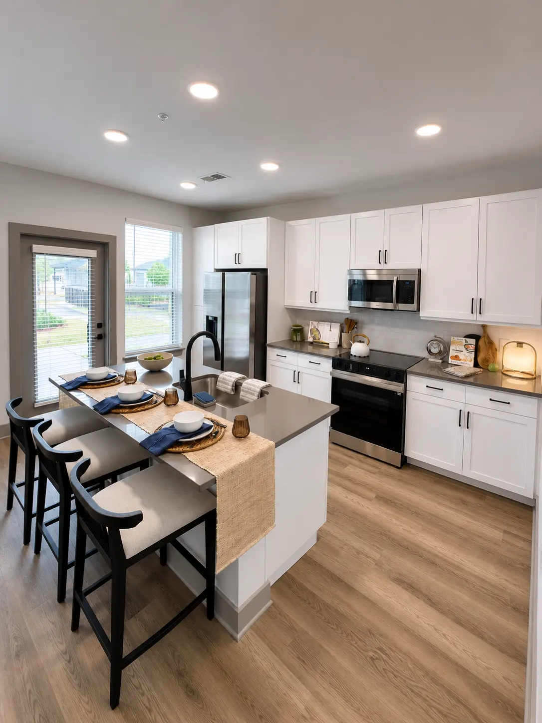 Modern Kitchen Interior A modern kitchen featuring white cabinetry, stainless steel appliances, and a large island with bar stools. Natural light fills the space through large windows.