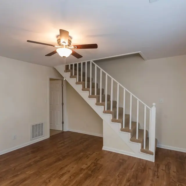 A spacious living room featuring hardwood flooring, a ceiling fan, and a staircase leading to the upper level.