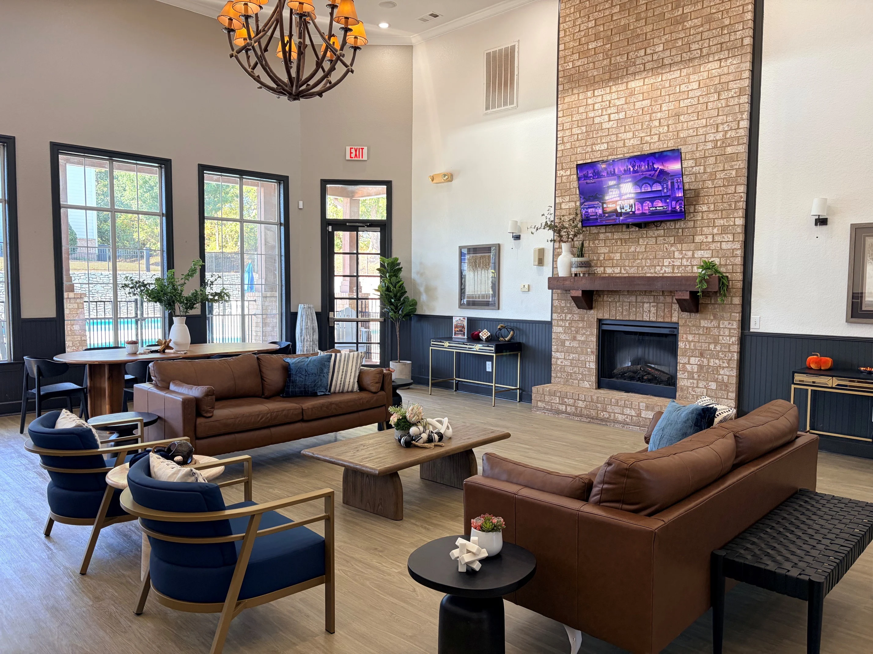 Stylish Community Lounge with Fireplace A spacious lounge area featuring comfortable seating arrangements including brown leather sofas and blue accent chairs. The area includes a large fireplace and a television mounted on the wall, with windows allowing natural light to fill the room.