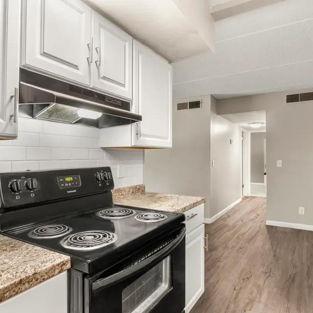 A modern kitchen featuring white cabinets, a black stove, and granite countertops. The image includes a glimpse of a hallway leading to another room.