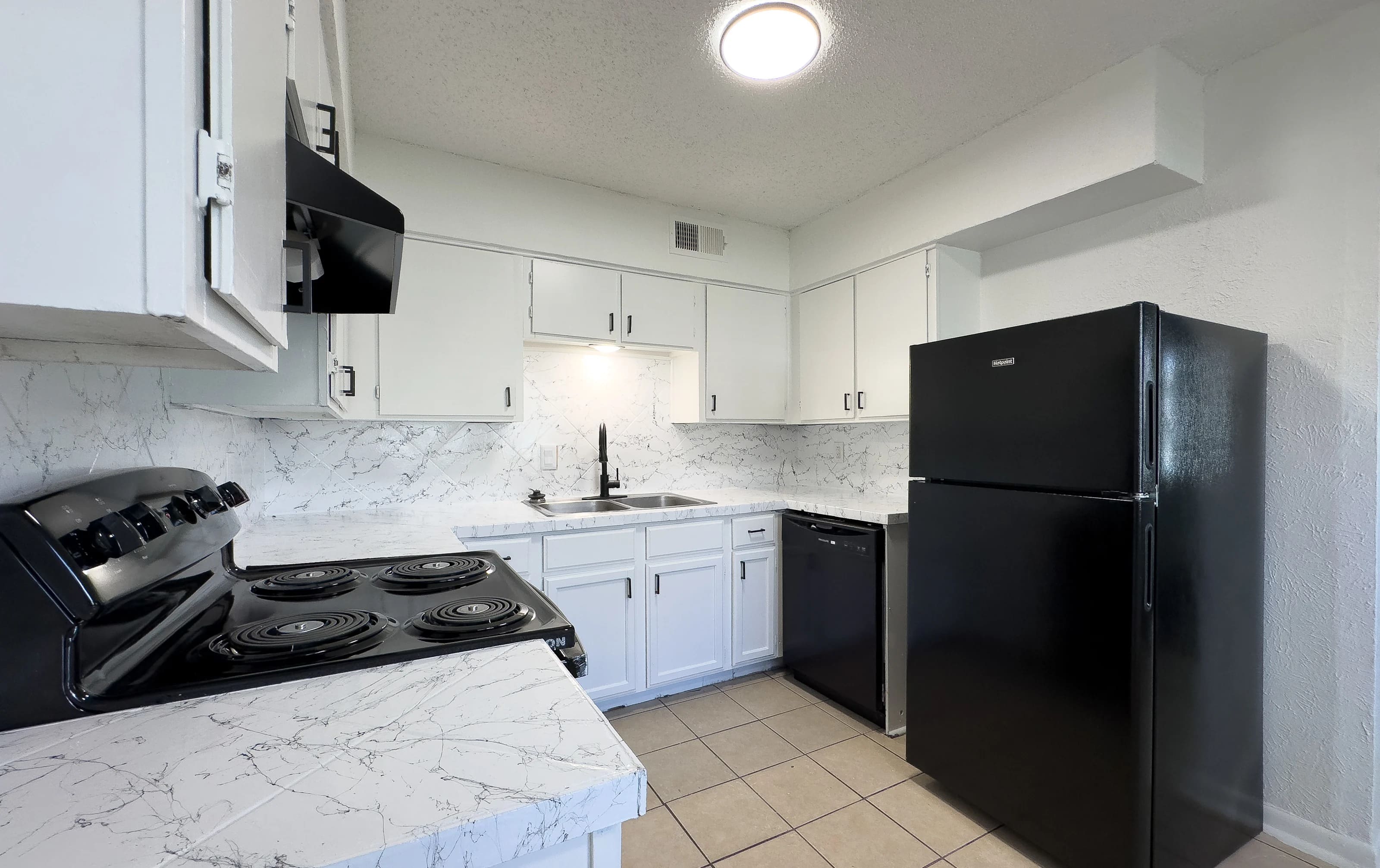 A modern kitchen featuring white cabinets, a black refrigerator, and a black stove with a marble countertop and tiled floor.