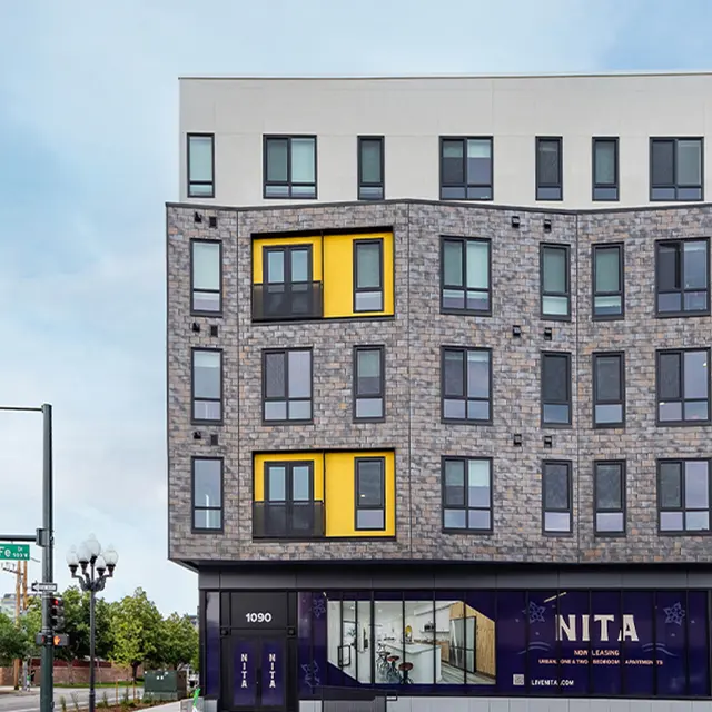 Contemporary Apartment Building A modern apartment building exterior featuring a mix of stone and colored panels with large windows.