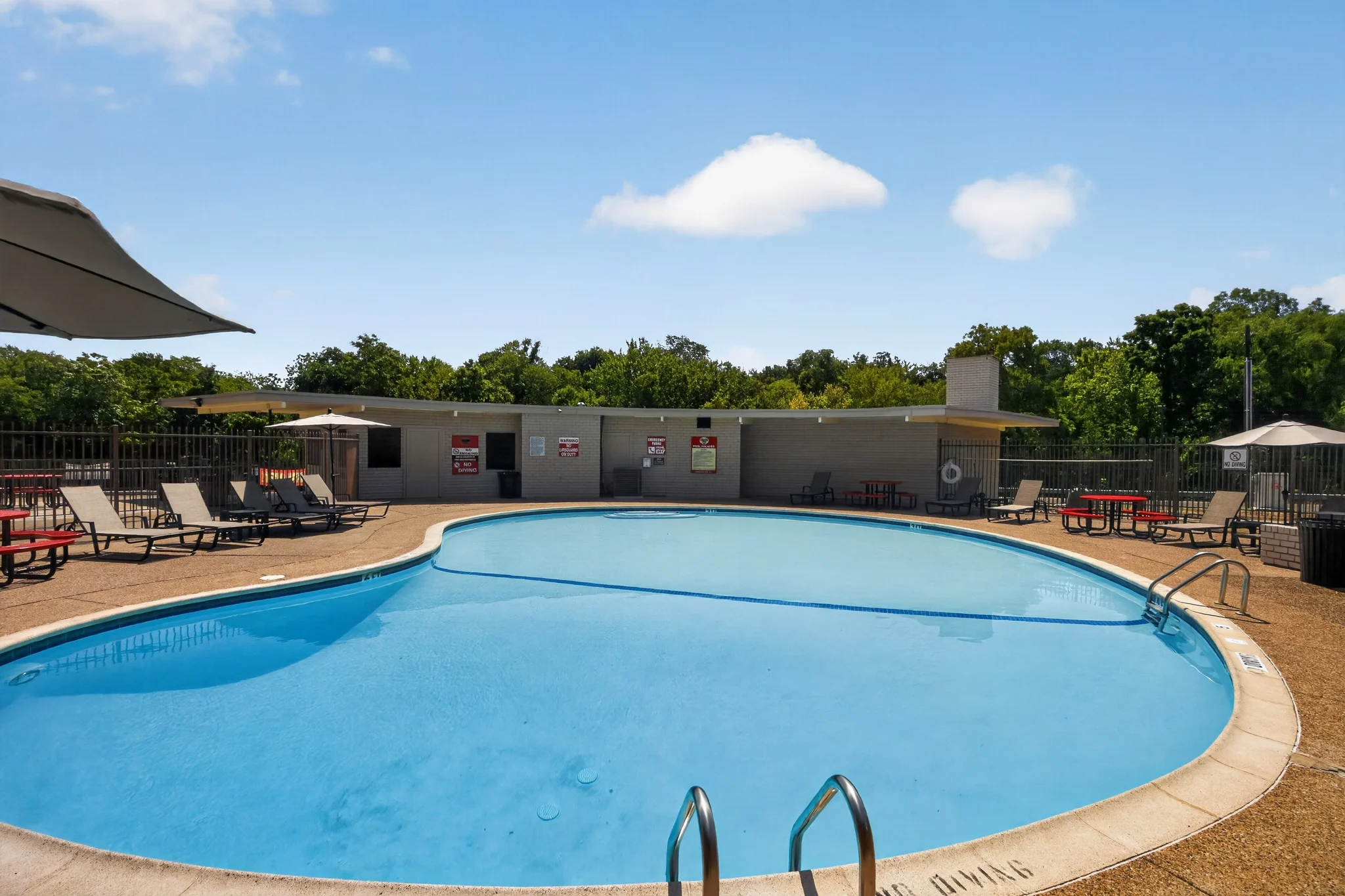 A swimming pool surrounded by lounge chairs in a community area with green trees in the background.