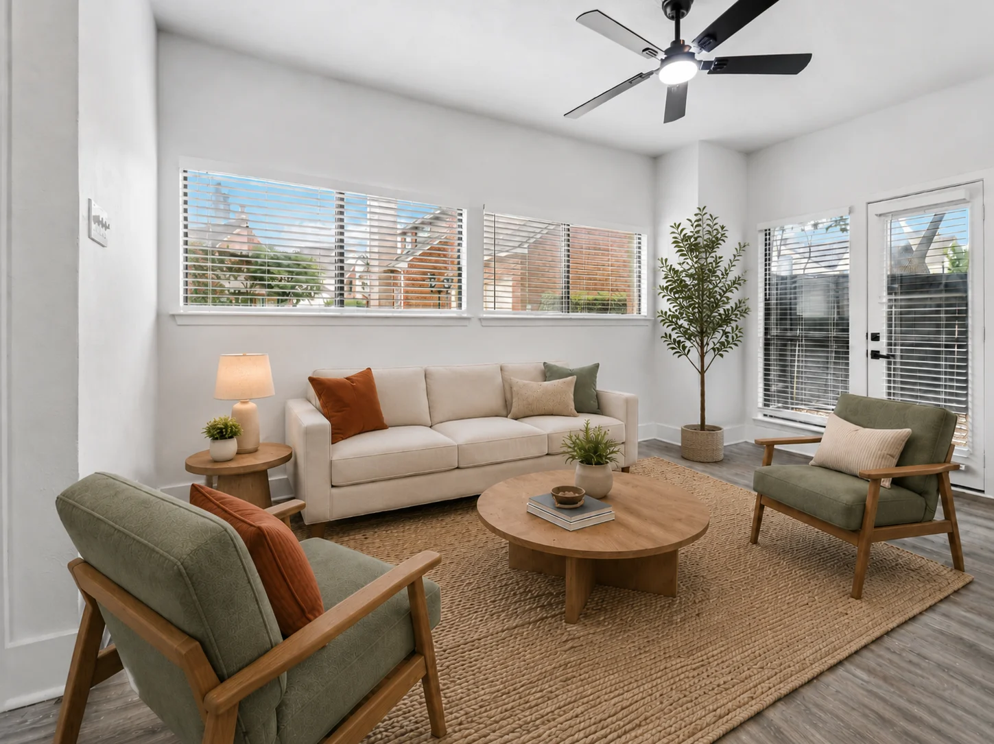 Modern Living Room Design A modern living room featuring a light-colored sofa, two green armchairs, a round wooden coffee table, and a textured area rug. There are large windows with blinds, a potted plant, and a floor lamp present.