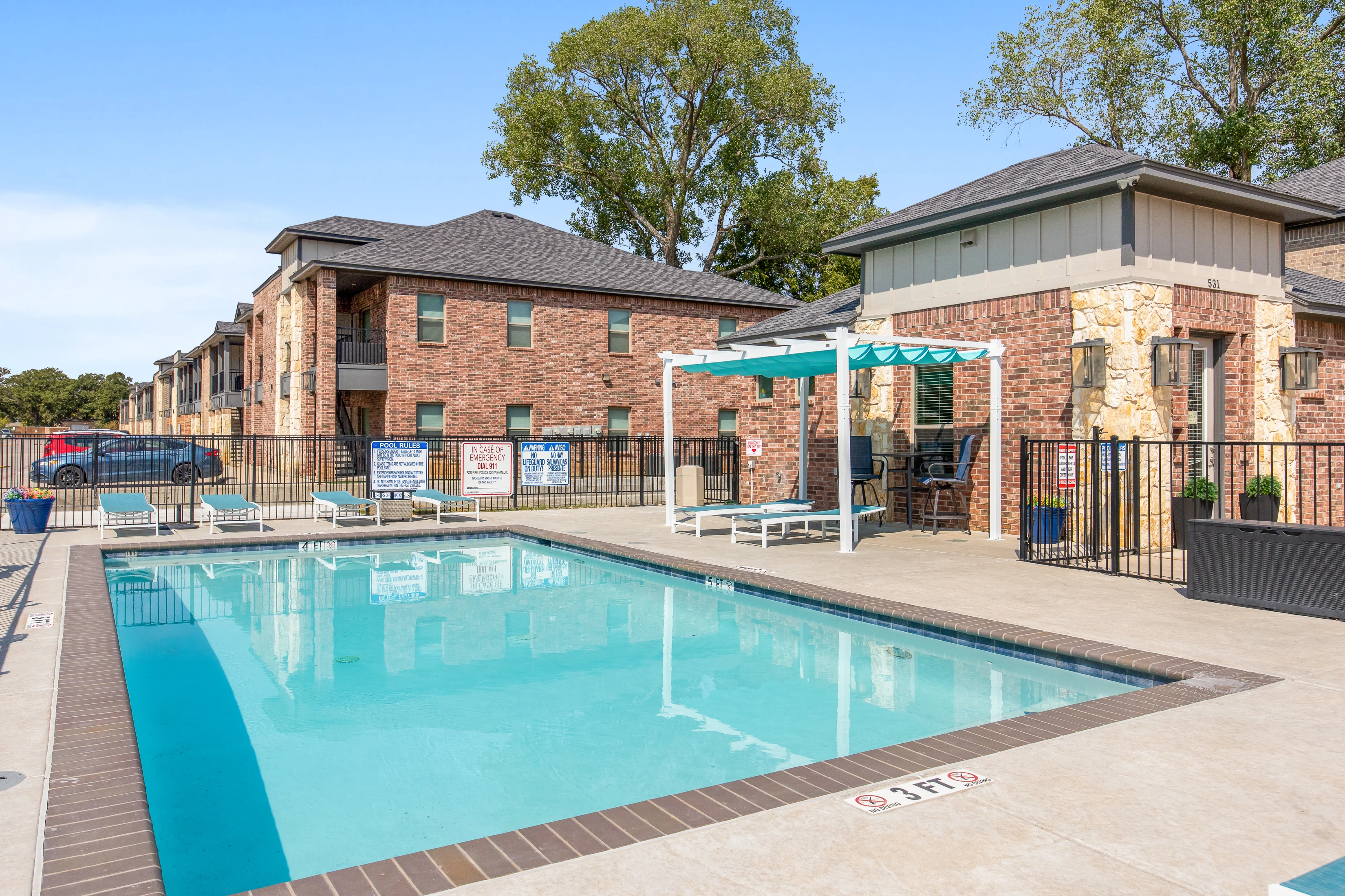 View of a swimming pool with lounge chairs and a cabana, surrounded by apartment buildings.