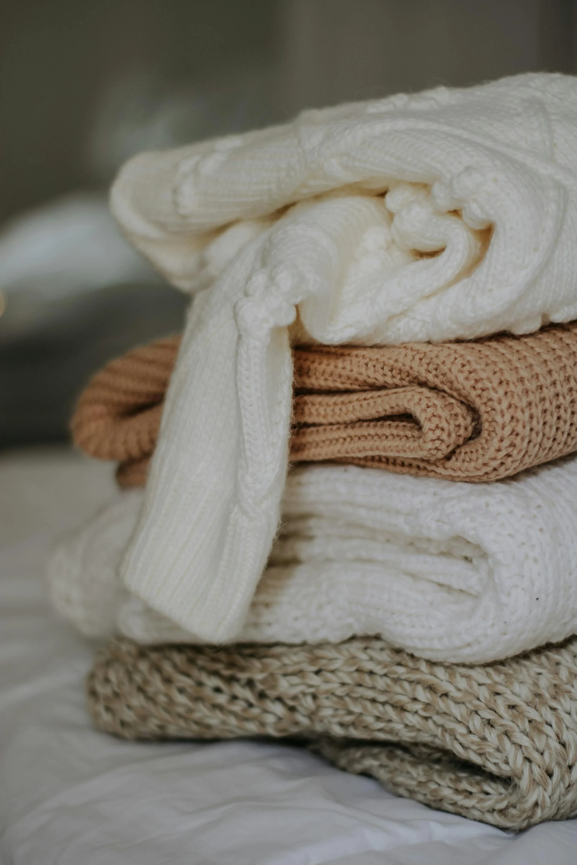 Stacked Knit Blankets A stack of neatly folded knit blankets in shades of cream, beige, and tan.