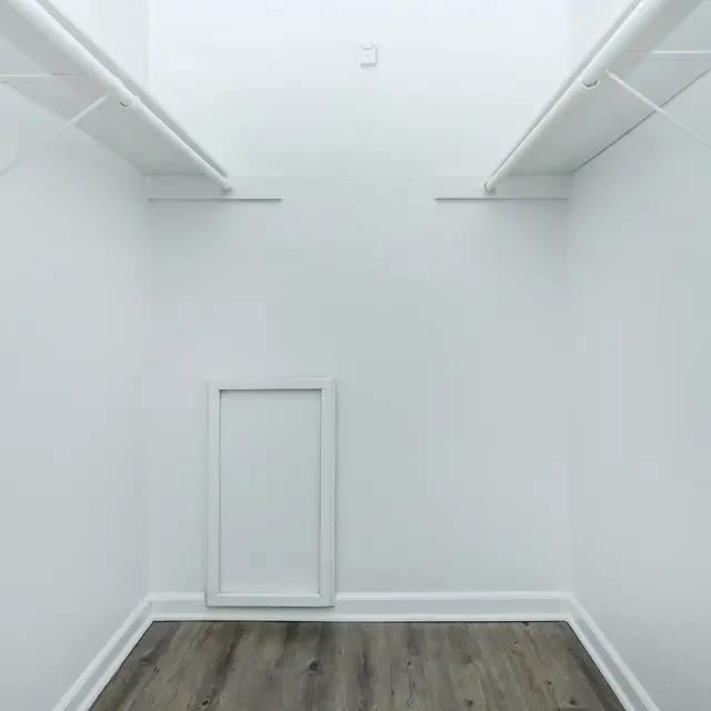 An empty closet with white walls and two shelves. A small framed opening is visible on the floor.