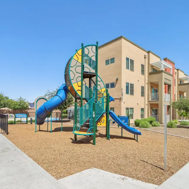 Playground with slide and climbing structure in an apartment complex courtyard under a clear blue sky.