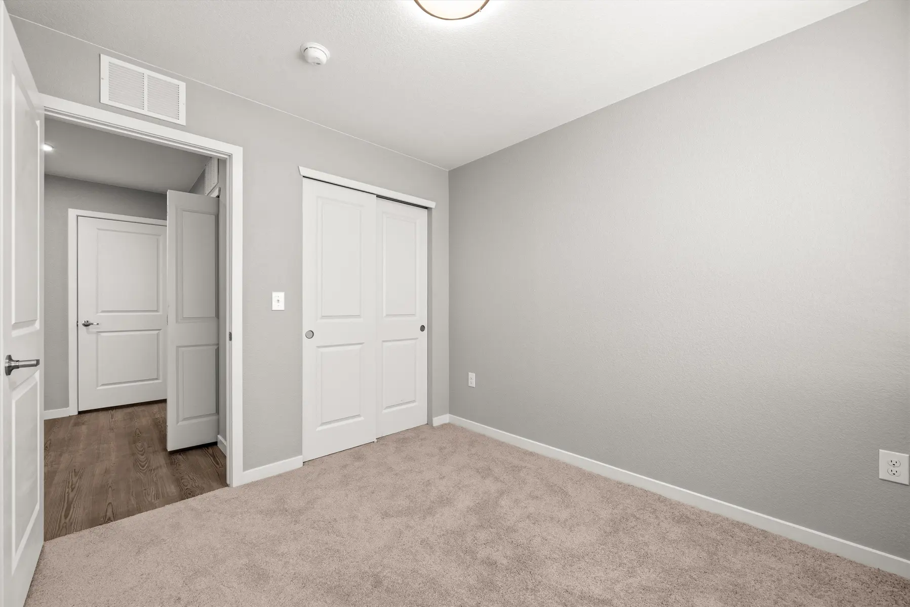 Empty Room Design An empty room with light grey walls and carpeted floor. Two closet doors are visible on the right, with a doorway leading to another room on the left.