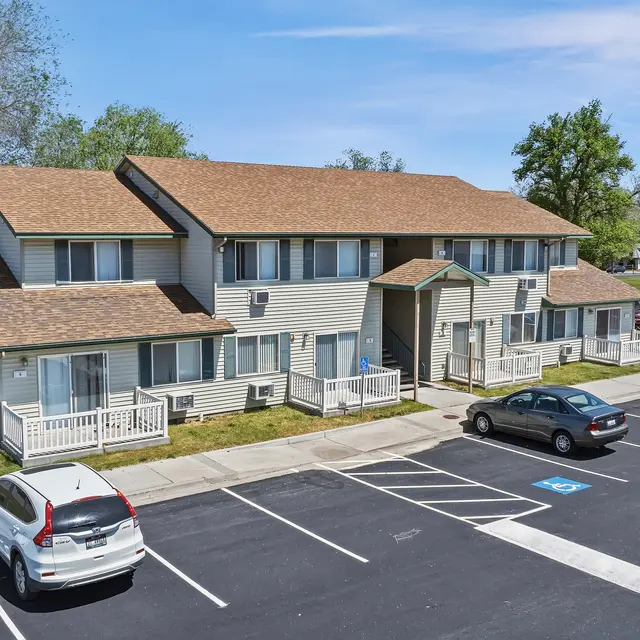 Aerial View of Apartment Complex Aerial view of a two-story apartment complex with a parking area in front. The buildings have multiple entrances and are surrounded by grass and trees.