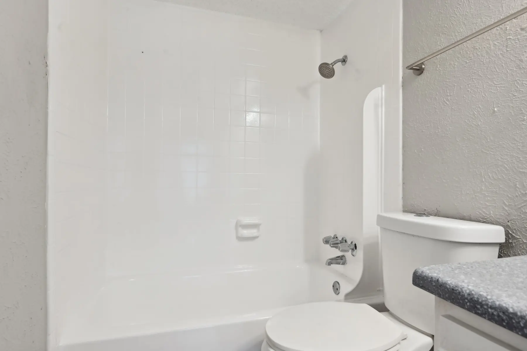 A clean, bright bathroom featuring a white shower and bathtub combination, a toilet, and a countertop with a sink.