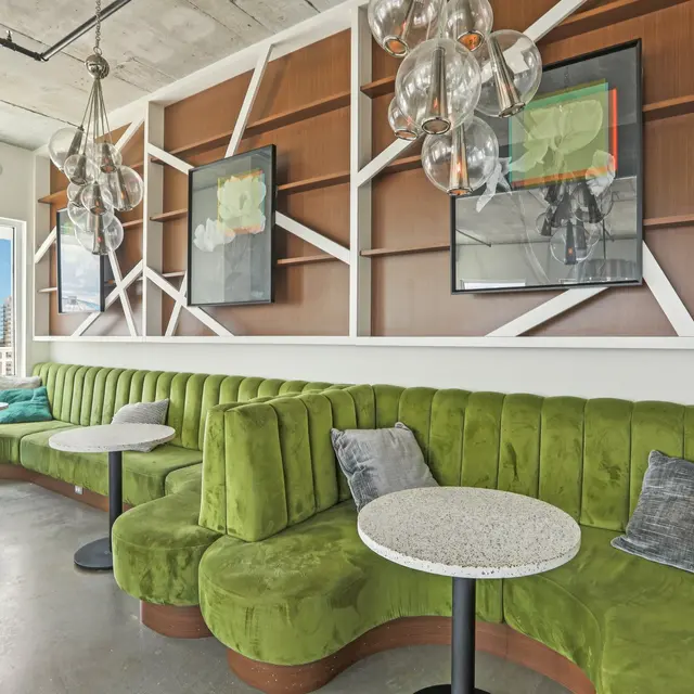 A modern lounge area featuring green upholstered seating, small round tables, and pendant lighting.